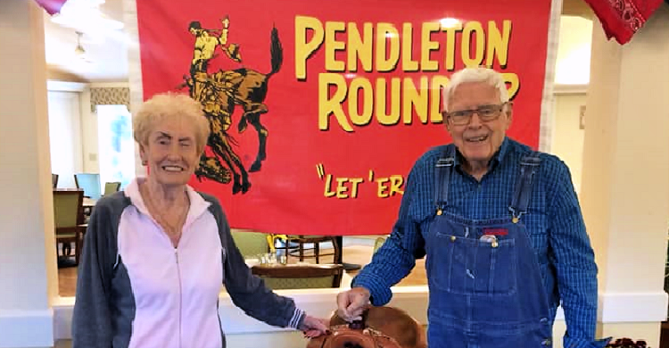 Elderly couple smiling in front of the Pendleton RoundUp saddle at Juniper House Assisted Living & Memory Care